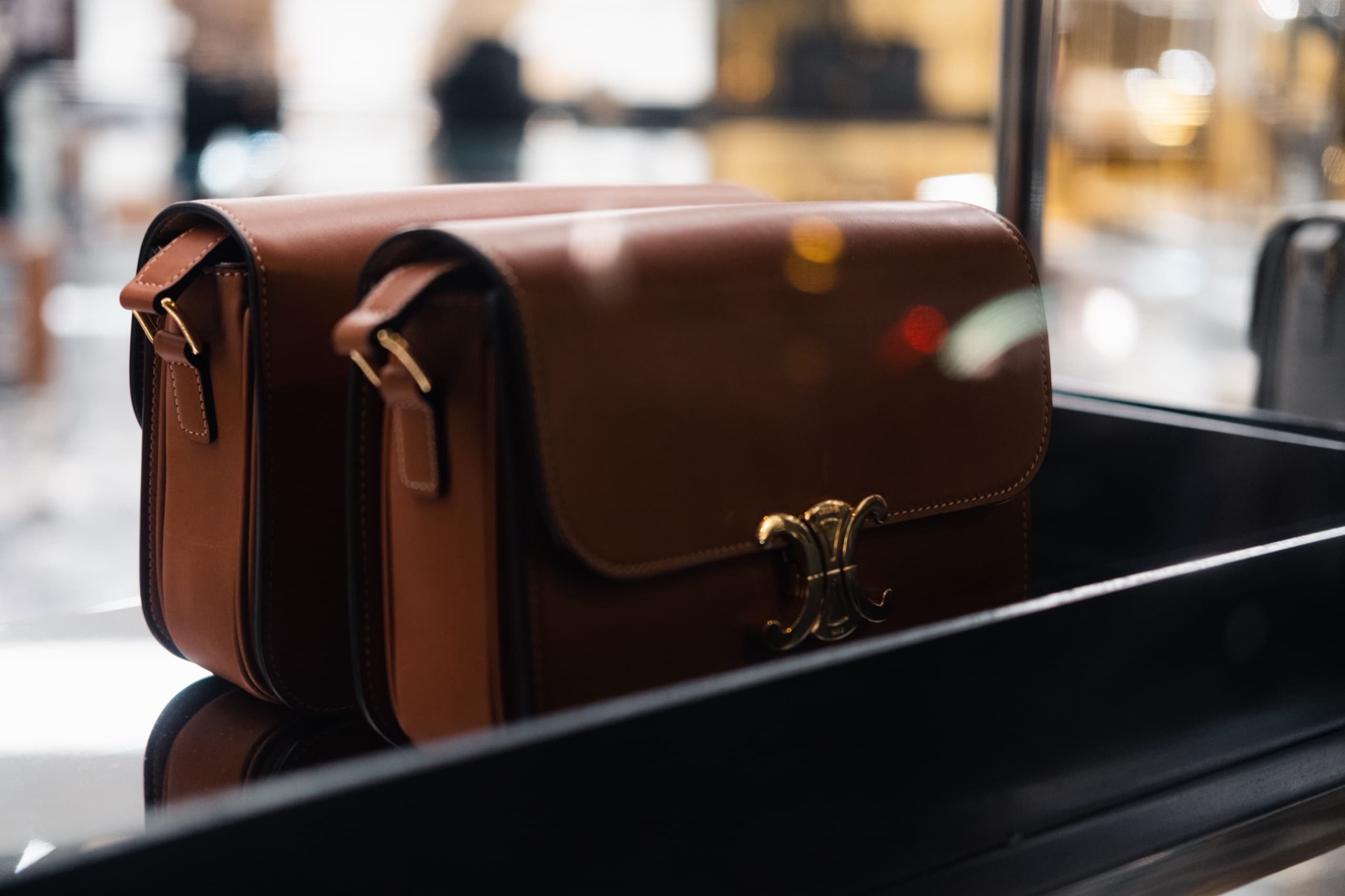 A tan leather shoulder bag with gold hardware displayed in a softly lit boutique window