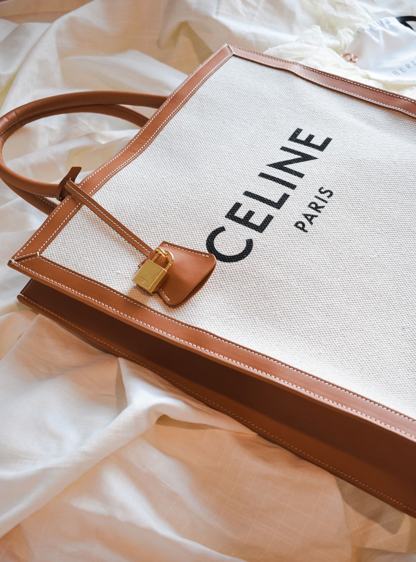 A Celine canvas tote with tan leather trim resting on cream linen